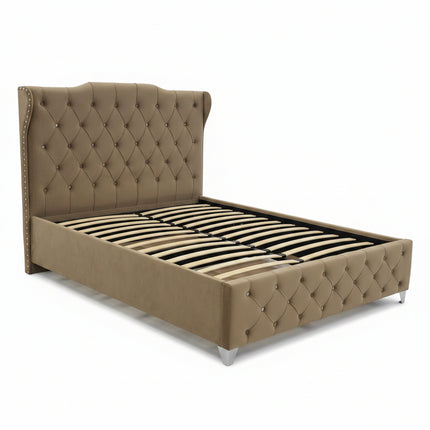 A beige upholstered bed frame with a tall tufted headboard and slatted base, photographed in a furniture showroom with other beds and mattresses visible in the background.