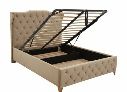 A tufted beige upholstered bed frame with a lift-up headboard and open storage base, photographed in a furniture showroom with other beds and showroom fixtures visible.