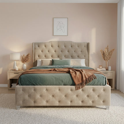 A tufted upholstered ottoman divan bed frame in a warm beige/taupe velvet, styled with sage green bedding and a brown throw blanket in a modern, softly lit bedroom.